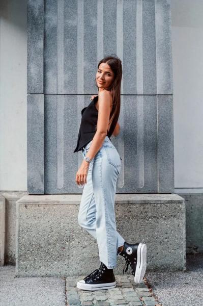 Девушка в светлых джинсах, черном топе и высоких кедах на платформе